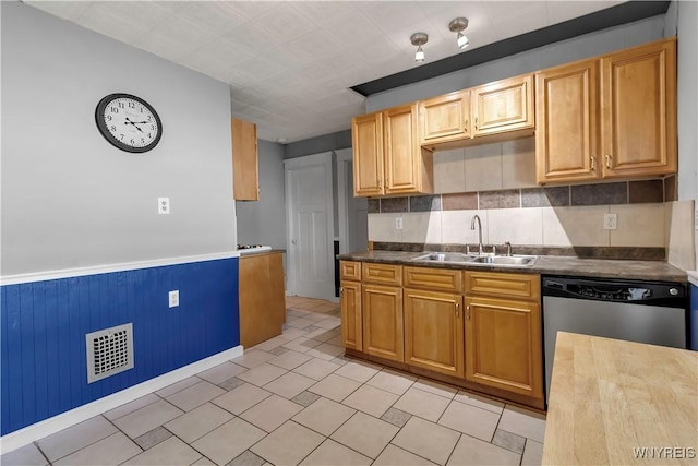 kitchen with dark countertops, a sink, a wainscoted wall, stainless steel dishwasher, and visible vents
