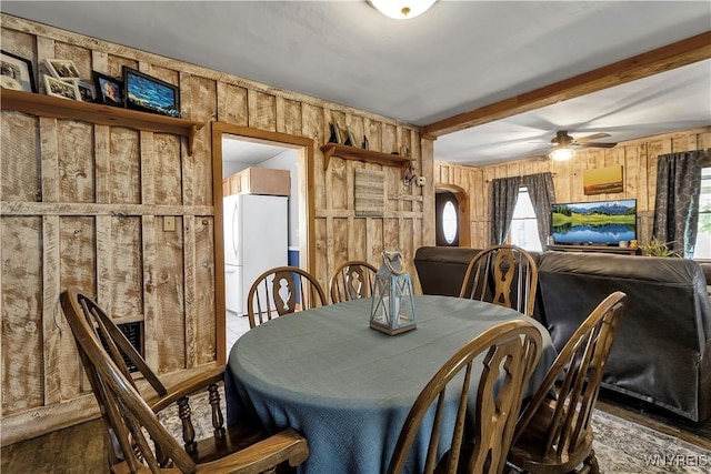 dining area with beamed ceiling, ceiling fan, wood walls, and wood finished floors