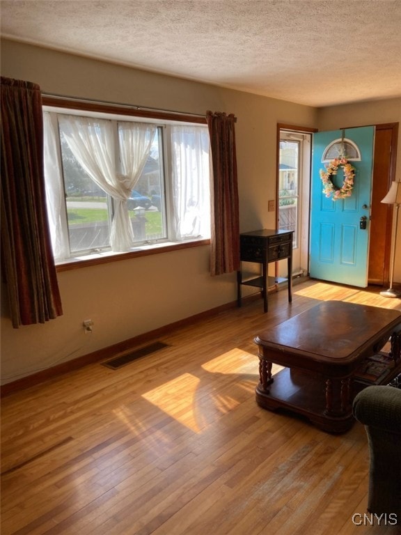 living room with light wood-style flooring, visible vents, a textured ceiling, and a healthy amount of sunlight