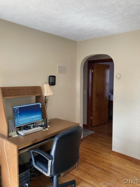 office area featuring arched walkways, wood finished floors, a textured ceiling, and baseboards