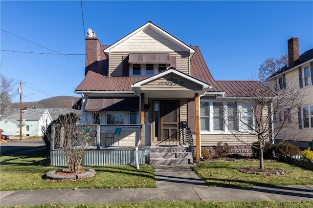 view of front facade with covered porch, a chimney, metal roof, and a front lawn