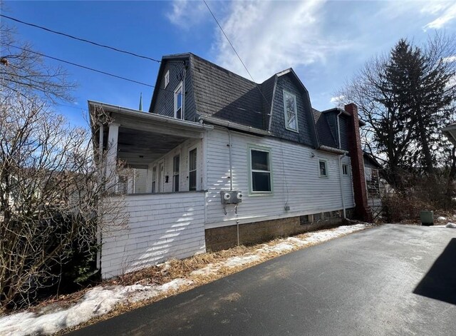 view of home's exterior with a gambrel roof, a chimney, and a shingled roof
