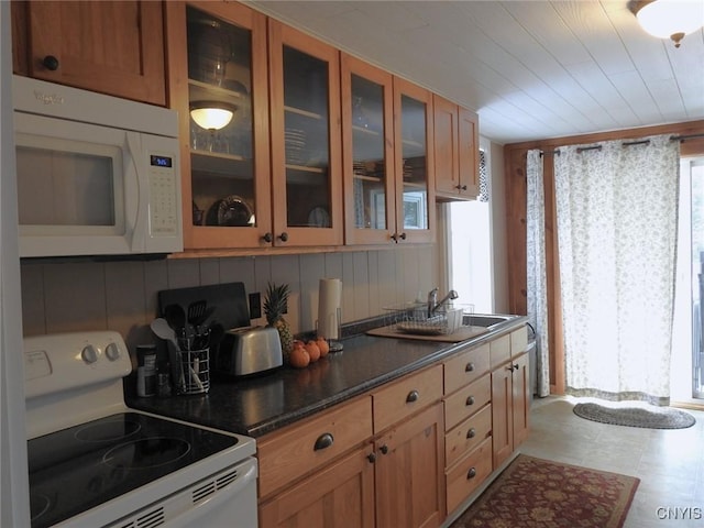 kitchen featuring white appliances, decorative backsplash, a sink, dark countertops, and glass insert cabinets