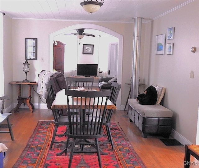 dining area with wood finished floors, crown molding, arched walkways, and a ceiling fan