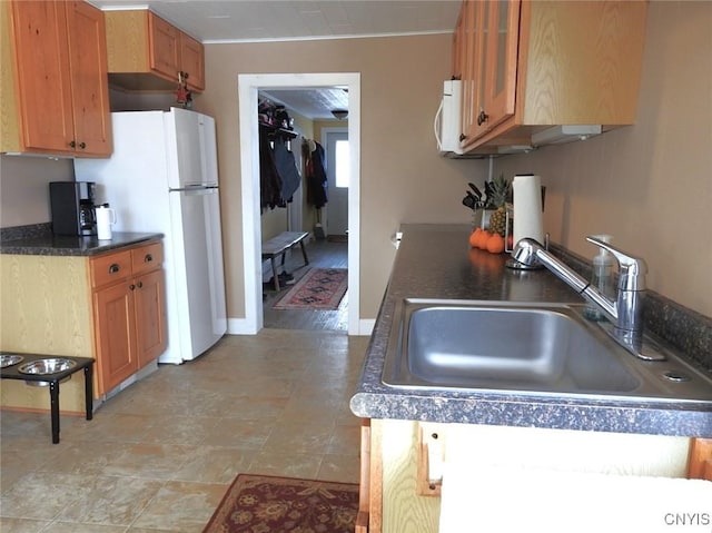 kitchen with brown cabinets, dark countertops, white appliances, and a sink