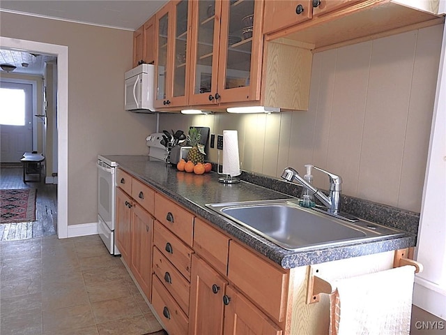 kitchen featuring white appliances, baseboards, dark countertops, glass insert cabinets, and a sink
