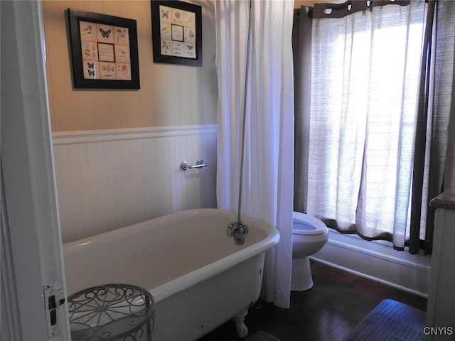 bathroom featuring a soaking tub, wainscoting, and toilet