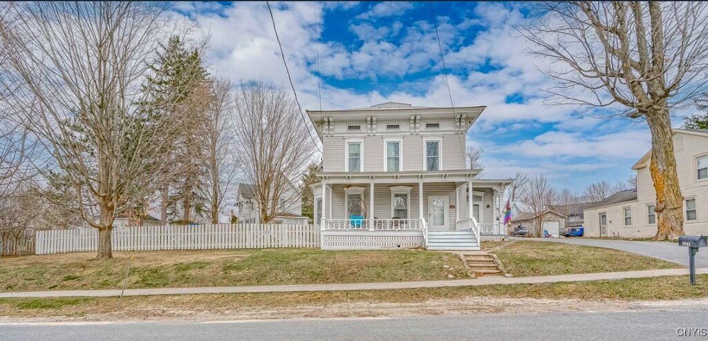 italianate house with a porch, fence, and a front lawn