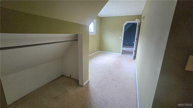 corridor featuring baseboards, a textured ceiling, vaulted ceiling, and light carpet
