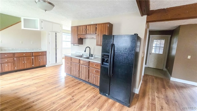 kitchen with a textured ceiling, beamed ceiling, a sink, black refrigerator with ice dispenser, and brown cabinetry