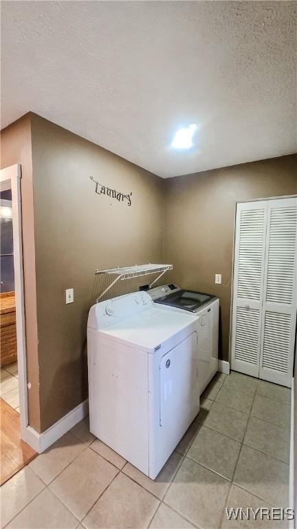 washroom featuring a textured ceiling, baseboards, laundry area, separate washer and dryer, and light tile patterned floors