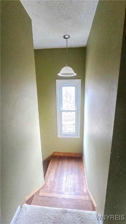 staircase with baseboards, wood finished floors, and a textured ceiling