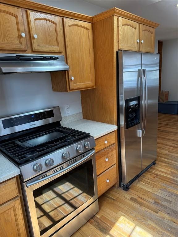 507 W Hudson St, Elmira-City, NY 14904 - kitchen featuring light countertops, brown cabinets, appliances with stainless steel finishes, under cabinet range hood, and light wood-type flooring