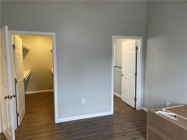 bedroom with dark wood finished floors, baseboards, and a walk in closet