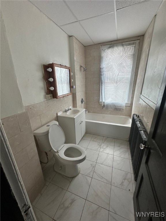 bathroom with radiator, marble finish floor, a drop ceiling, toilet, and tile walls