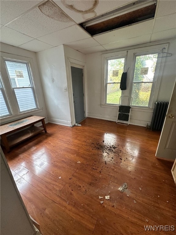empty room featuring radiator, baseboards, wood-type flooring, and a drop ceiling
