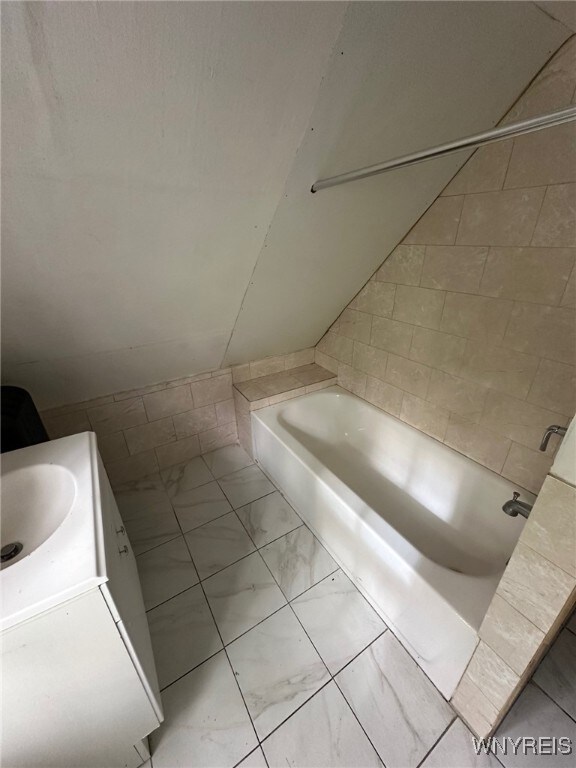 full bathroom featuring marble finish floor, a tub, and a sink
