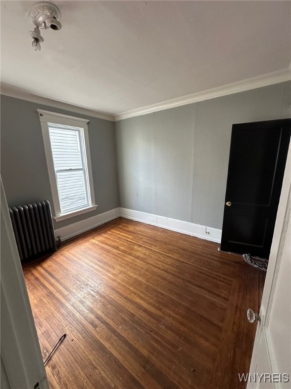 unfurnished room featuring radiator, baseboards, crown molding, and wood finished floors