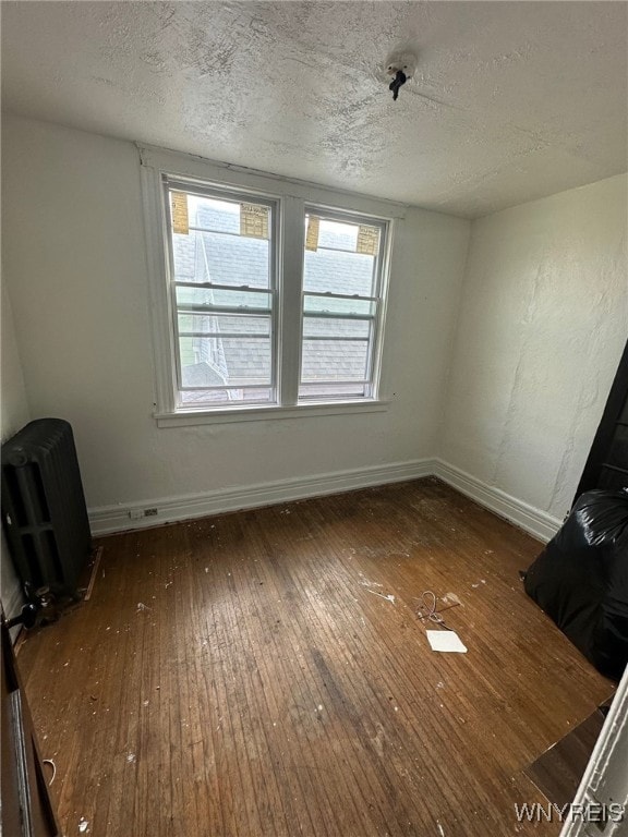 spare room with radiator heating unit, hardwood / wood-style floors, a textured ceiling, and baseboards