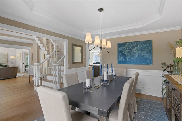 dining area featuring stairway, wood finished floors, ornamental molding, and a tray ceiling