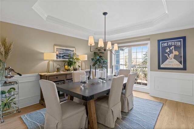 dining room featuring wood finished floors, crown molding, a tray ceiling, and wainscoting