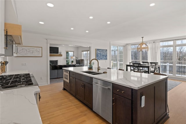 kitchen featuring appliances with stainless steel finishes, dark brown cabinetry, light wood finished floors, and a sink