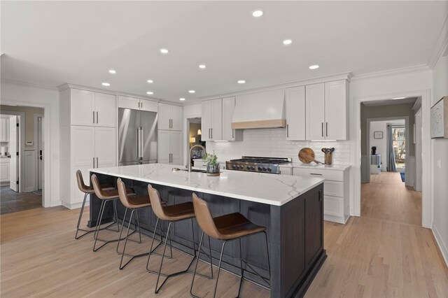 kitchen featuring a sink, high end refrigerator, ornamental molding, premium range hood, and white cabinets