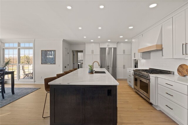 kitchen with custom range hood, appliances with stainless steel finishes, a sink, white cabinetry, and a kitchen breakfast bar
