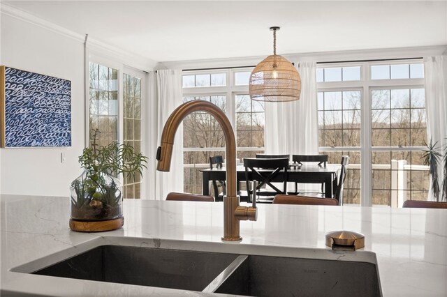 interior space featuring ornamental molding, a sink, decorative light fixtures, and light stone counters