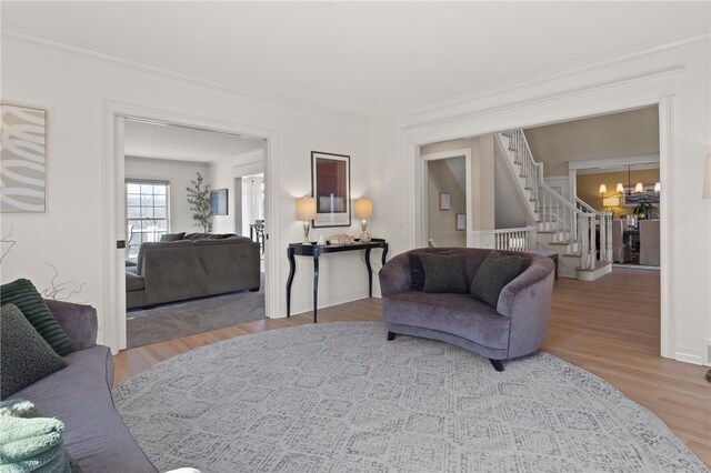 living room featuring stairway, wood finished floors, an inviting chandelier, and crown molding