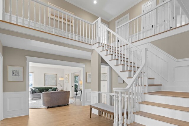 stairway with recessed lighting, a high ceiling, a decorative wall, wainscoting, and wood finished floors