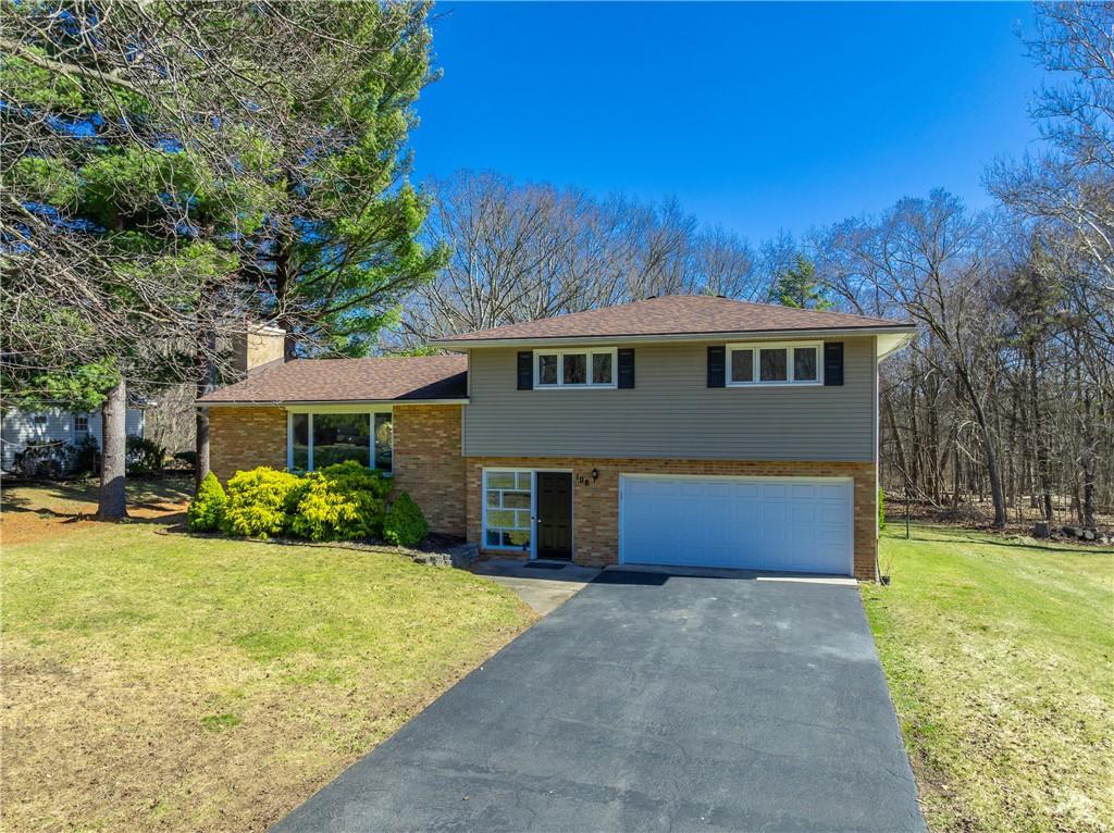 split level home with an attached garage, driveway, a front yard, brick siding, and a chimney