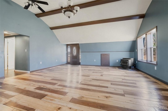 unfurnished living room featuring beam ceiling, a wood stove, baseboards, ceiling fan, and hardwood / wood-style floors