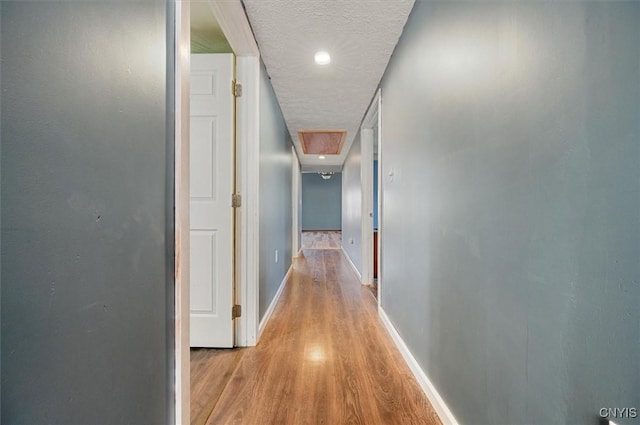 hall with baseboards, light wood-style floors, and a textured ceiling