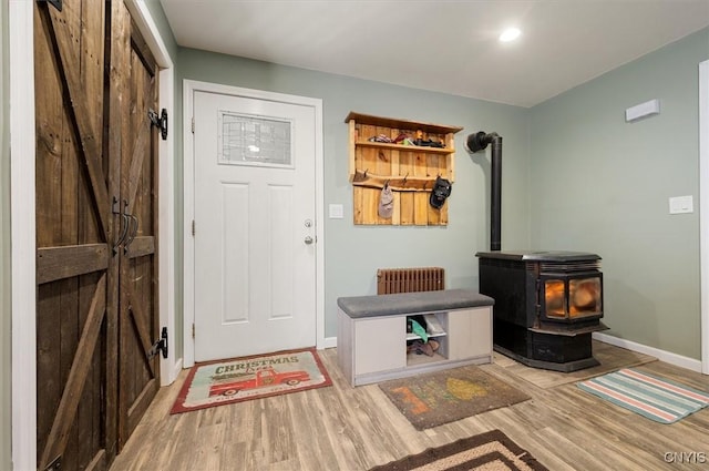 foyer with radiator heating unit, wood finished floors, baseboards, and a wood stove