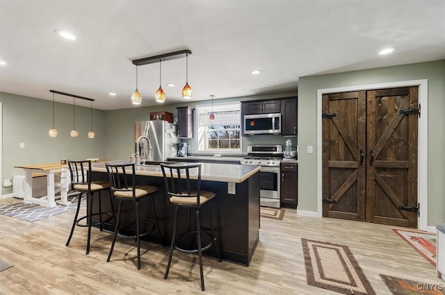 kitchen with a center island with sink, a breakfast bar area, light wood-style flooring, and appliances with stainless steel finishes