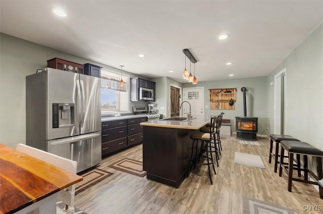kitchen featuring a sink, a kitchen breakfast bar, appliances with stainless steel finishes, light wood-style flooring, and a kitchen island with sink