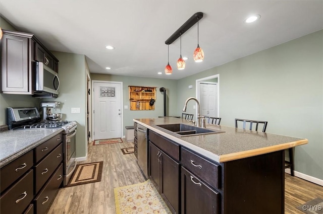 kitchen featuring light wood finished floors, a center island with sink, a sink, and stainless steel appliances