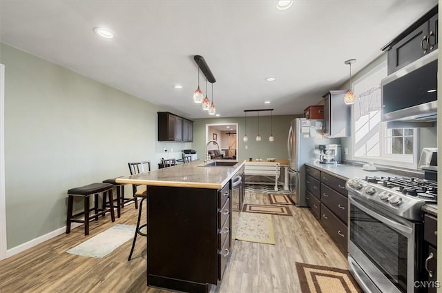 kitchen featuring light wood-style flooring, stainless steel appliances, an island with sink, a sink, and a kitchen breakfast bar