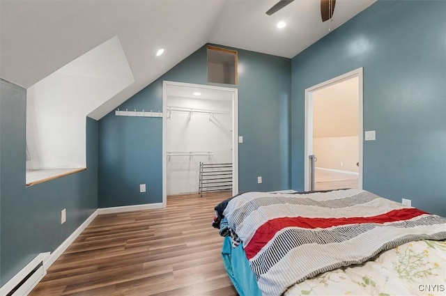 bedroom with a closet, baseboards, wood finished floors, a baseboard heating unit, and a spacious closet