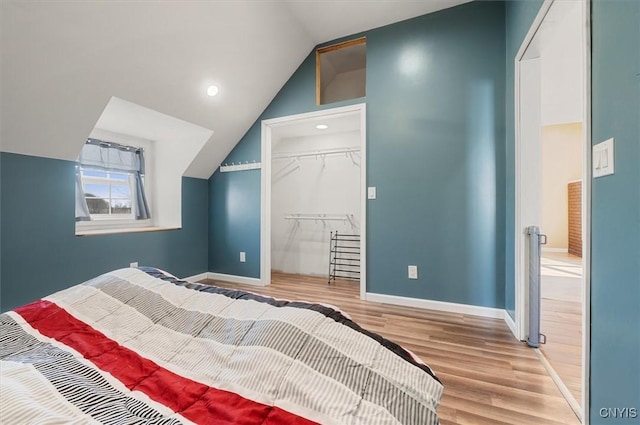 bedroom with a walk in closet, lofted ceiling, baseboards, a closet, and wood finished floors