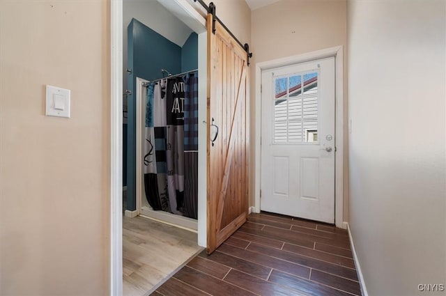 hall featuring baseboards, a barn door, and wood finish floors