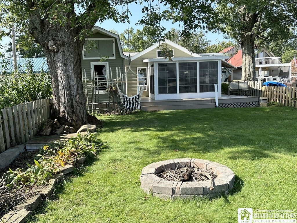 rear view of house with a sunroom, an outdoor fire pit, a fenced backyard, a deck, and a lawn