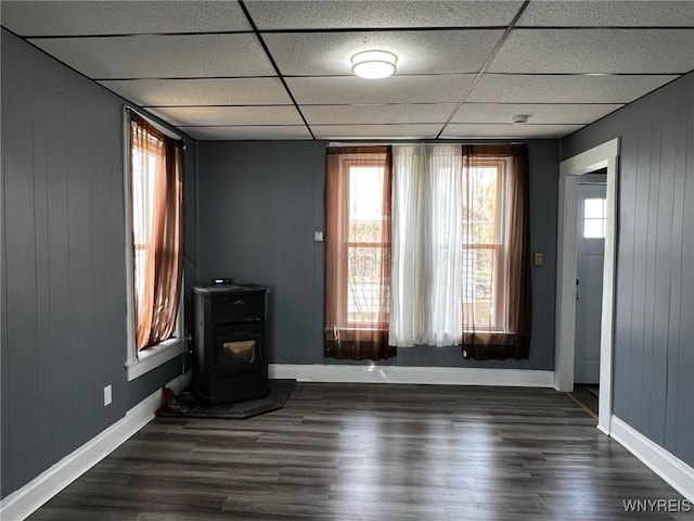 unfurnished living room featuring a drop ceiling, dark wood-style flooring, baseboards, and a wood stove