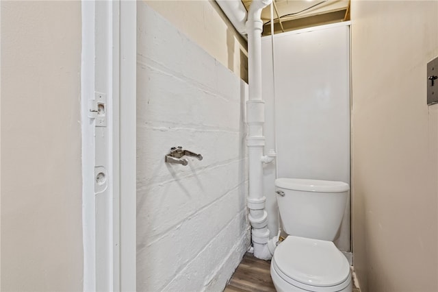 bathroom featuring concrete block wall, toilet, and wood finished floors