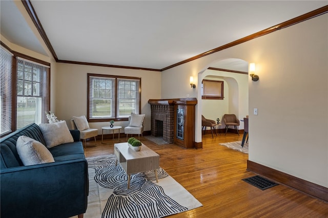living area with light wood finished floors, baseboards, visible vents, arched walkways, and ornamental molding