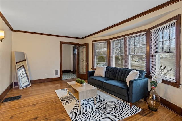 living room with baseboards, visible vents, crown molding, and wood finished floors