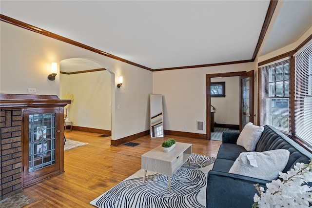 living room with crown molding, wood finished floors, baseboards, visible vents, and arched walkways