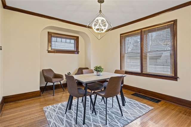 dining area featuring visible vents, baseboards, ornamental molding, arched walkways, and light wood-style floors
