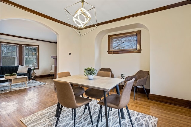 dining space with arched walkways, ornamental molding, and wood finished floors